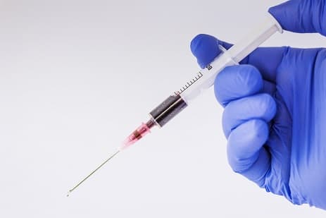 Syringe with red liquid in blue gloved hand
